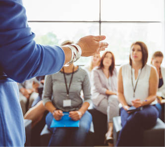 Hand of a trainer addressing group of females sitting in a conference hall  Female hand against defocused group of women attending seminar 